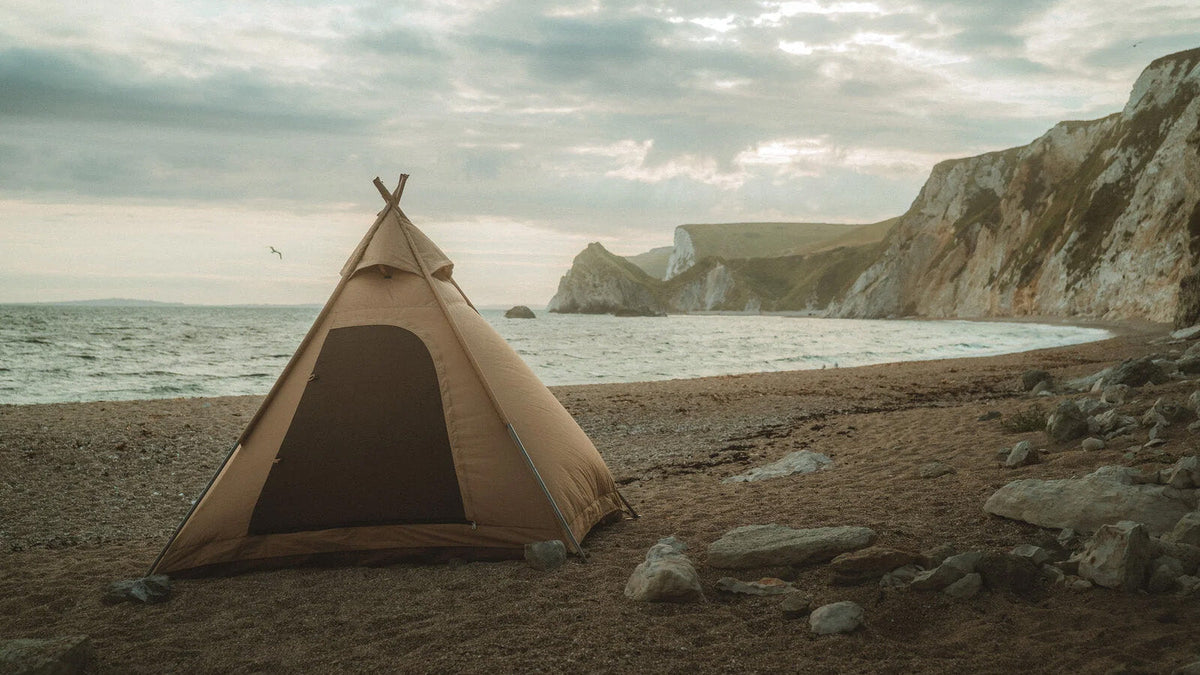 Tenten, beige tipitent met open deur op een kiezelstrand aan zee bij witte kliffen