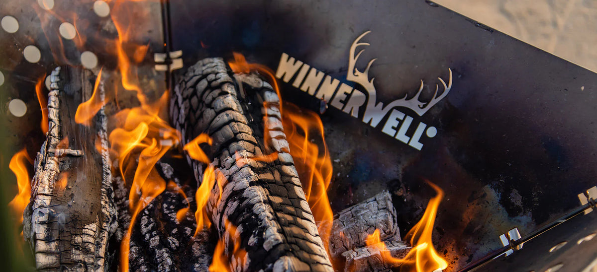 Winnerwell vuurkorf met brandende houtblokken en het uitgesneden Winnerwell logo met een gewei