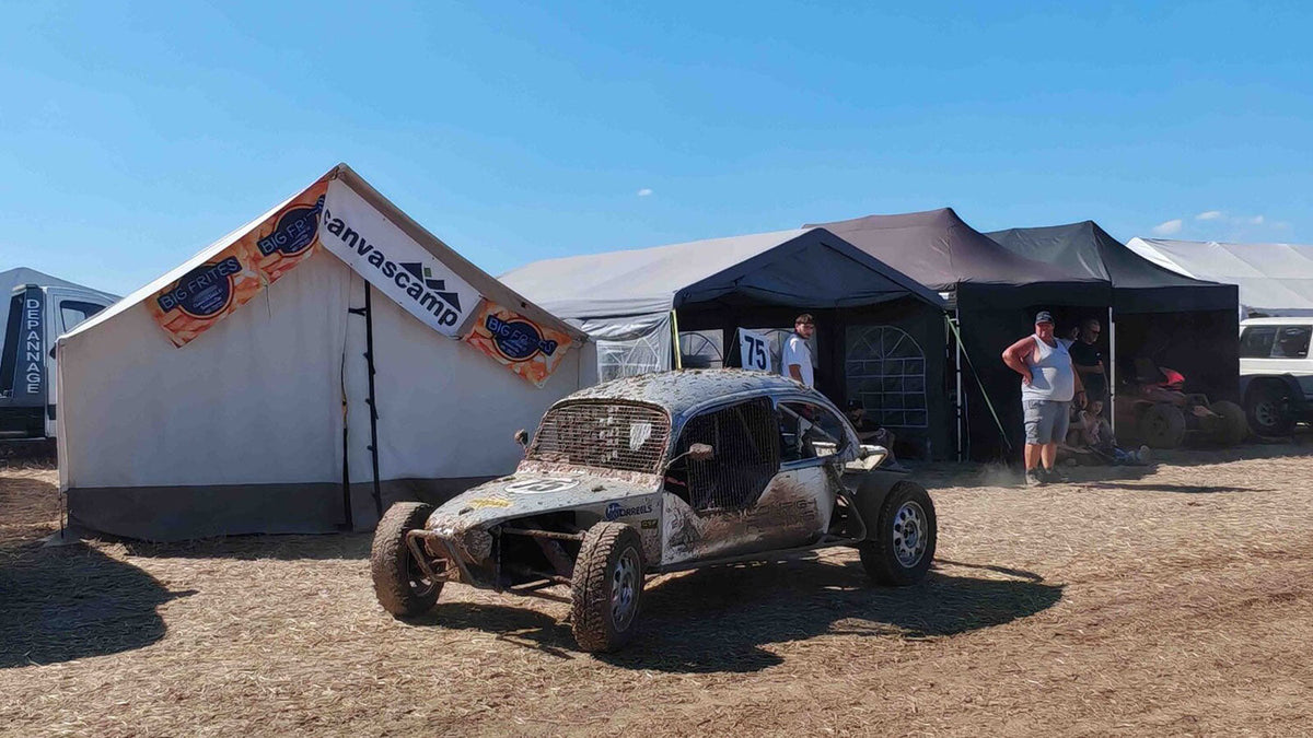 Safaritenten, witte tent met spandoek naast een modderige buggy op een stoffig terrein
