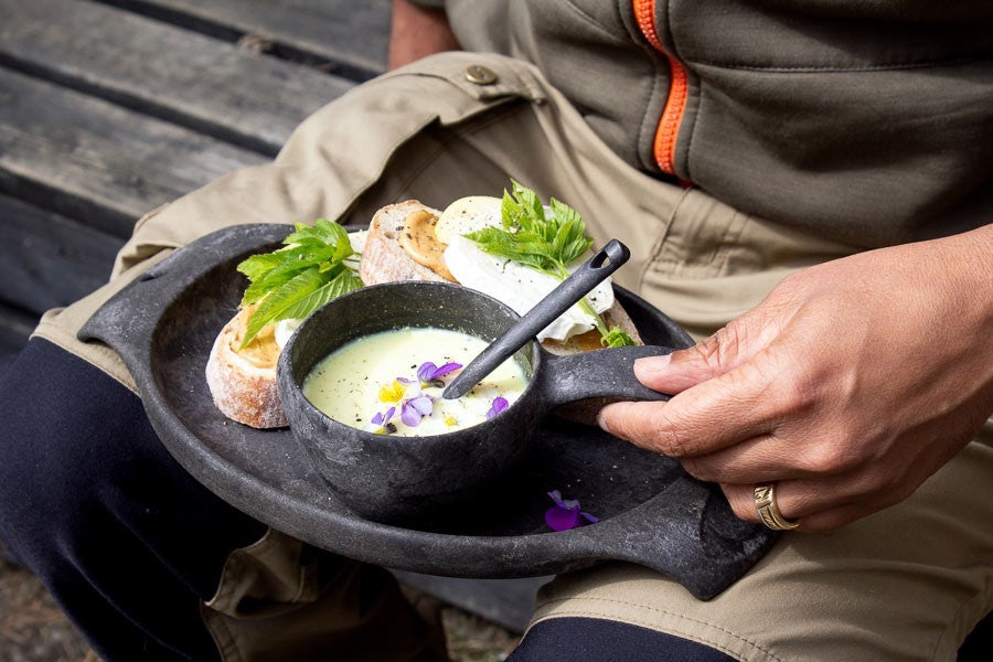Kupilka 21 Classic Cup noire avec soupe et cuillère sur une assiette noire avec des petits pains, sur les genoux