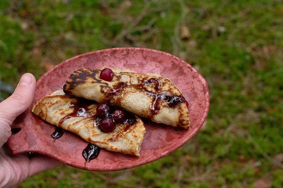 Kupilka 14 Petite Assiette rouge avec crêpes et cerises, tenue en main au-dessus de l'herbe