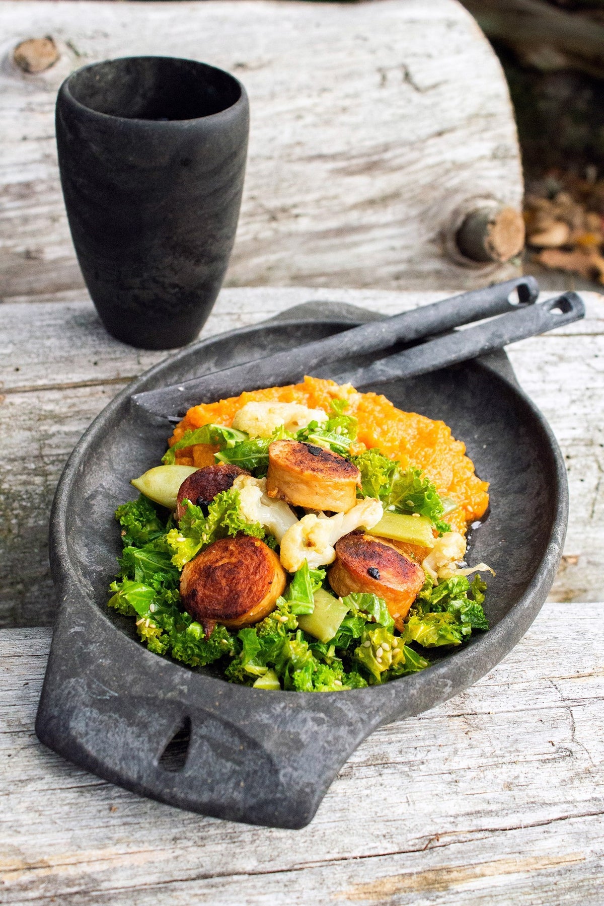 Kupilka 30 Coffee Go Cup noire à côté d'une assiette noire avec saucisses et légumes sur du bois