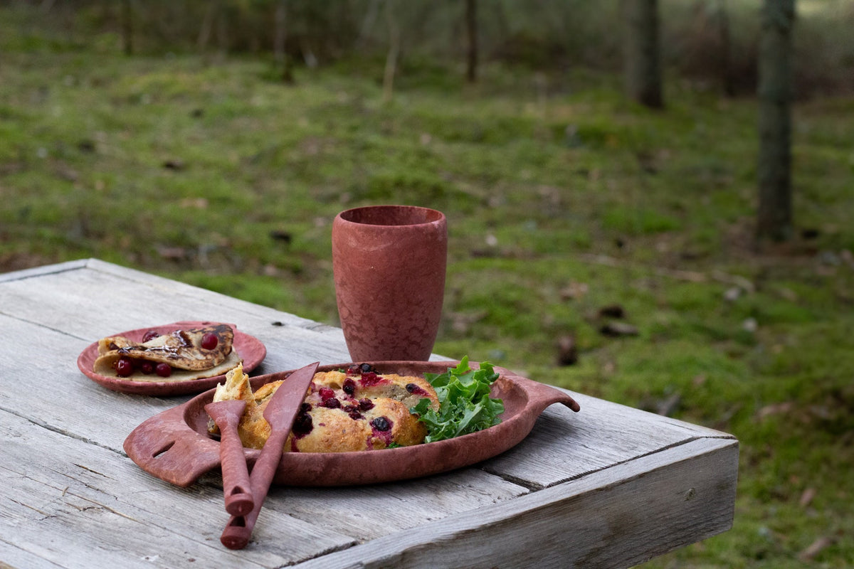 Kupilka 30 Coffee Go Cup rouge sur une table en bois en extérieur près d'assiettes rouges avec des plats