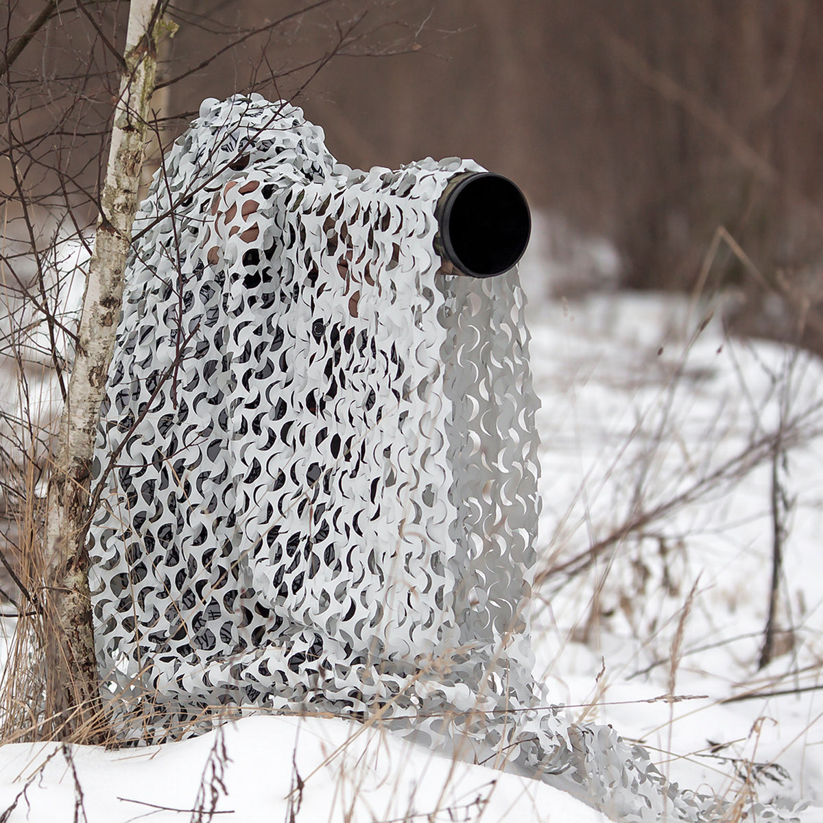 Filet de camouflage Buteo 3D Leafs Neige utilisé dans la neige, objectif qui dépasse du filet à droite