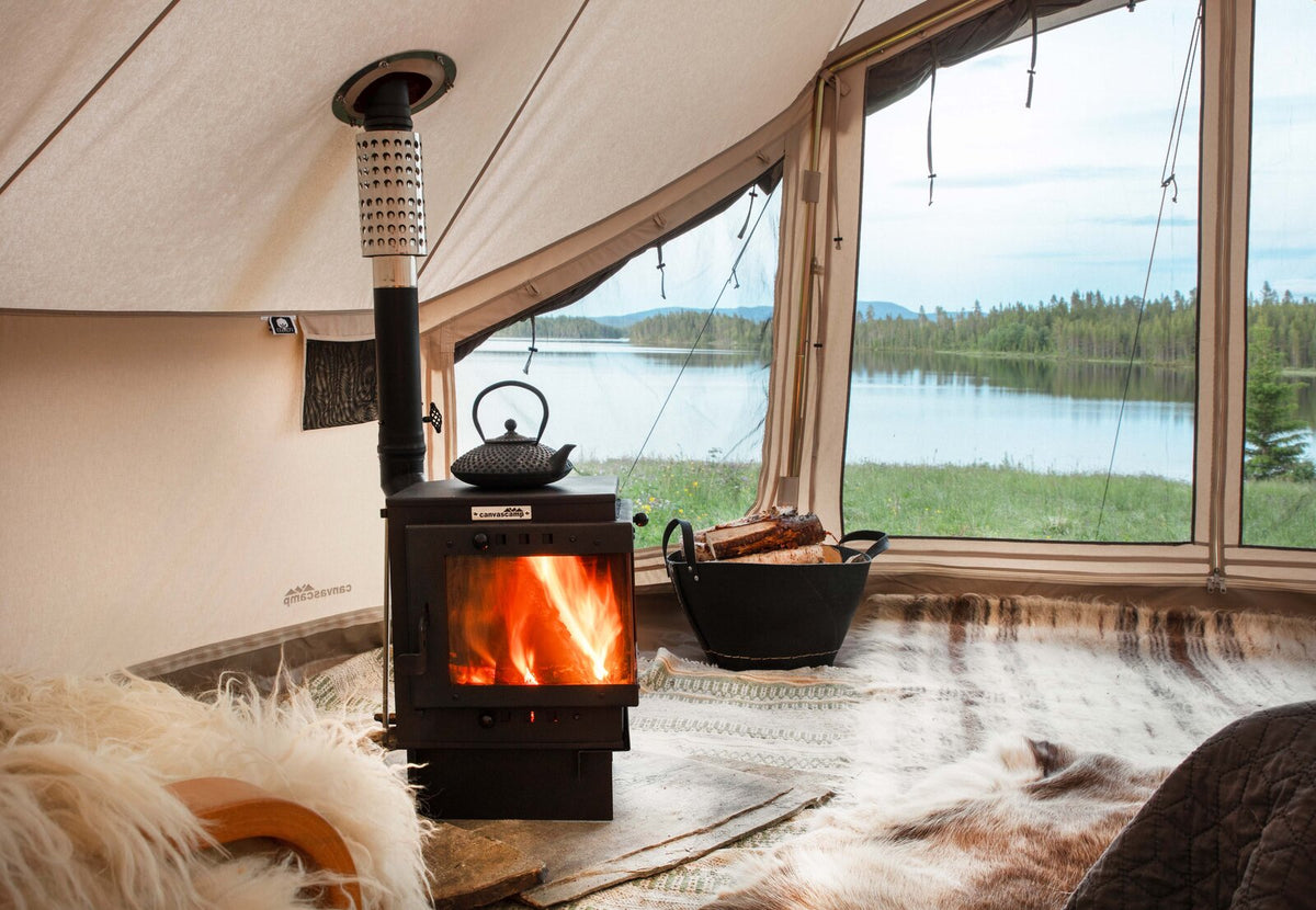 CanvasCamp Bison allumé avec une théière noire dessus, dans une tente avec vue sur un lac