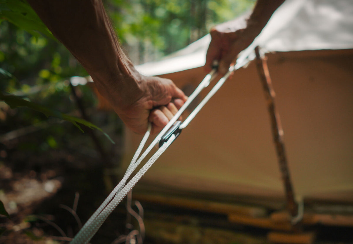 Hauban CanvasCamp avec tendeur, des mains tendent la corde à côté de la tente
