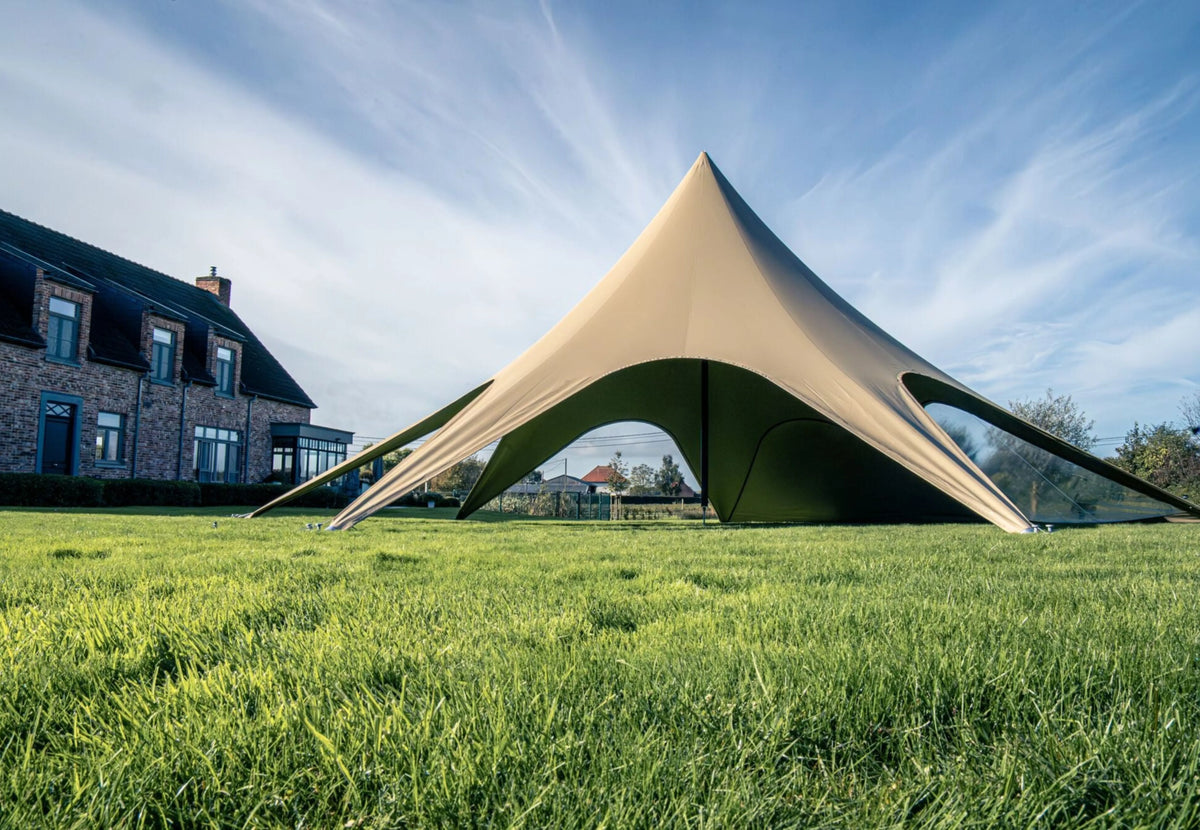 Tente événementielle CanvasCamp StarShade Pro vue au ras de l'herbe, avec une maison en briques derrière