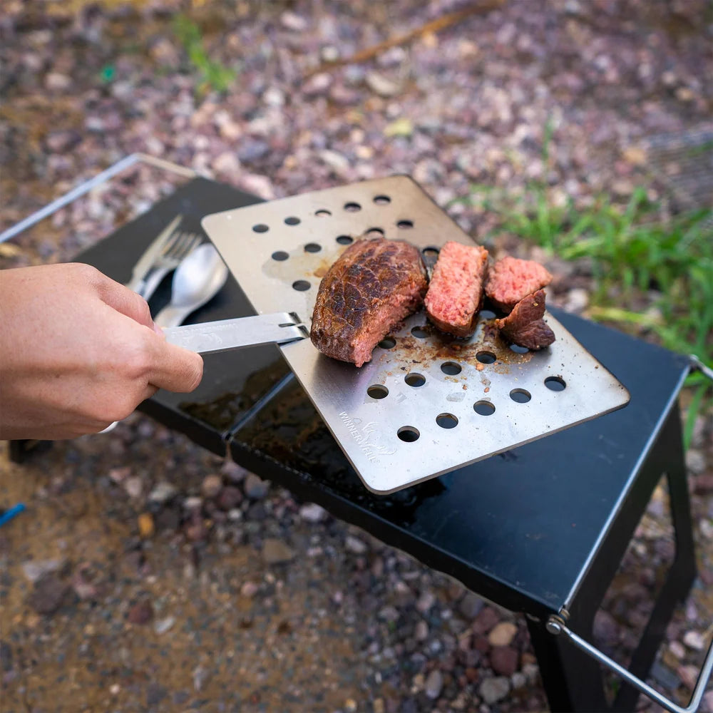 Plaque grill Winnerwell avec un steak tranché sur une petite table, une main tient le manche