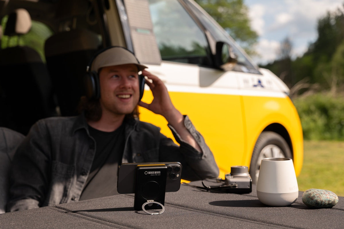 WakaWaka Power Pro avec un téléphone sur une table dehors, un homme avec un casque devant un van jaune