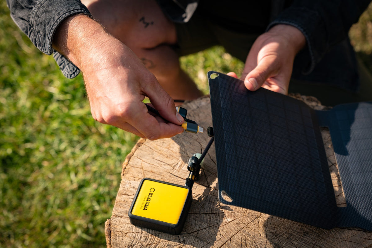 WakaWaka Solar 10 sur une souche d'arbre dans l'herbe, relié à une batterie externe jaune