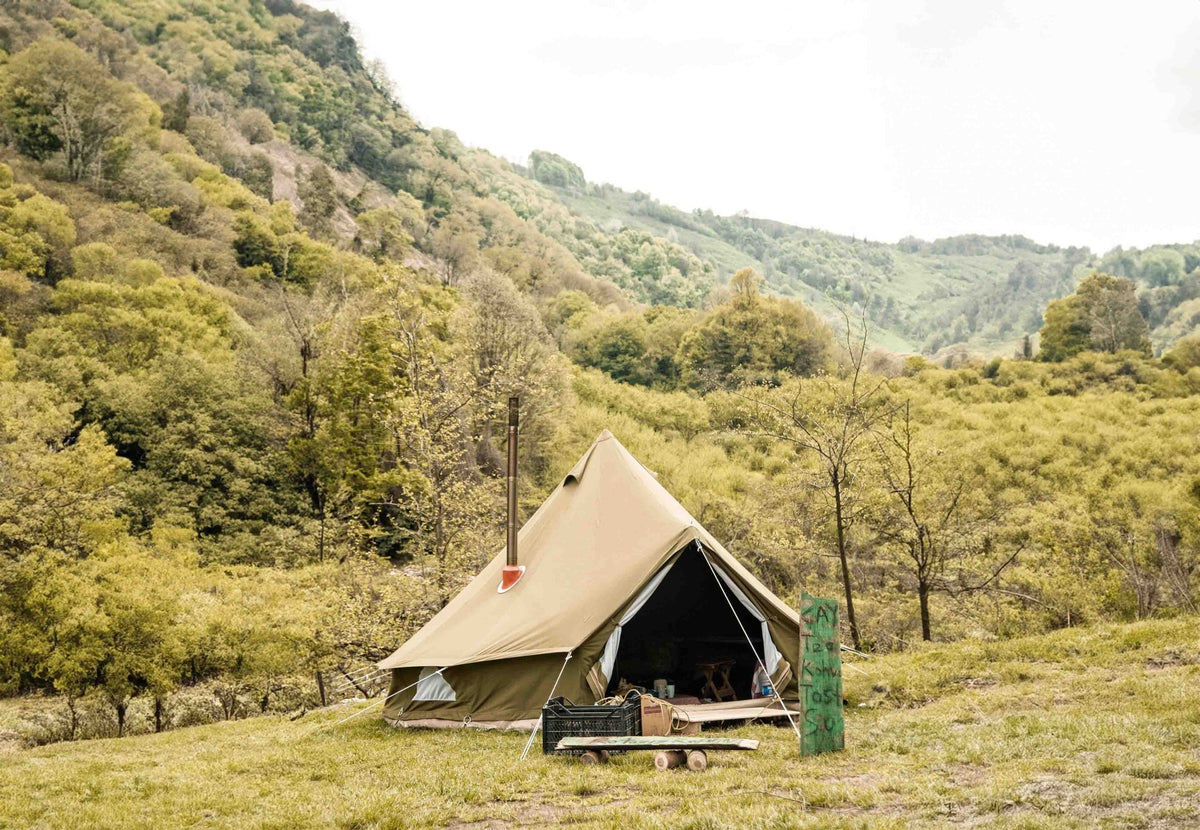 CanvasCamp Exit 45° sur une tente beige porte ouverte avec tuyau de poêle dans un paysage de montagne verdoyant