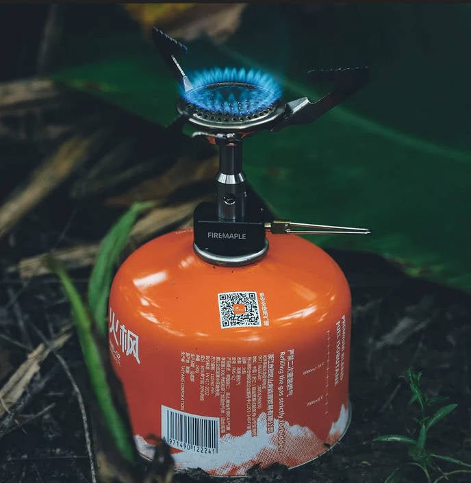 Fire Maple BUZZ sur une cartouche de gaz orange avec flamme bleue, dehors dans l'herbe