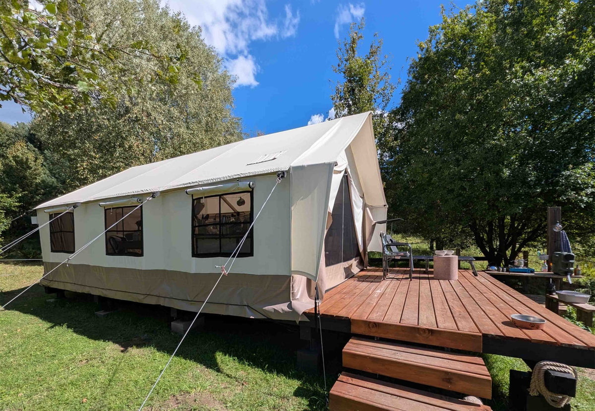 CanvasCamp Heavy Duty Safari Tent avec terrasse en bois et petit escalier dans un jardin ensoleillé