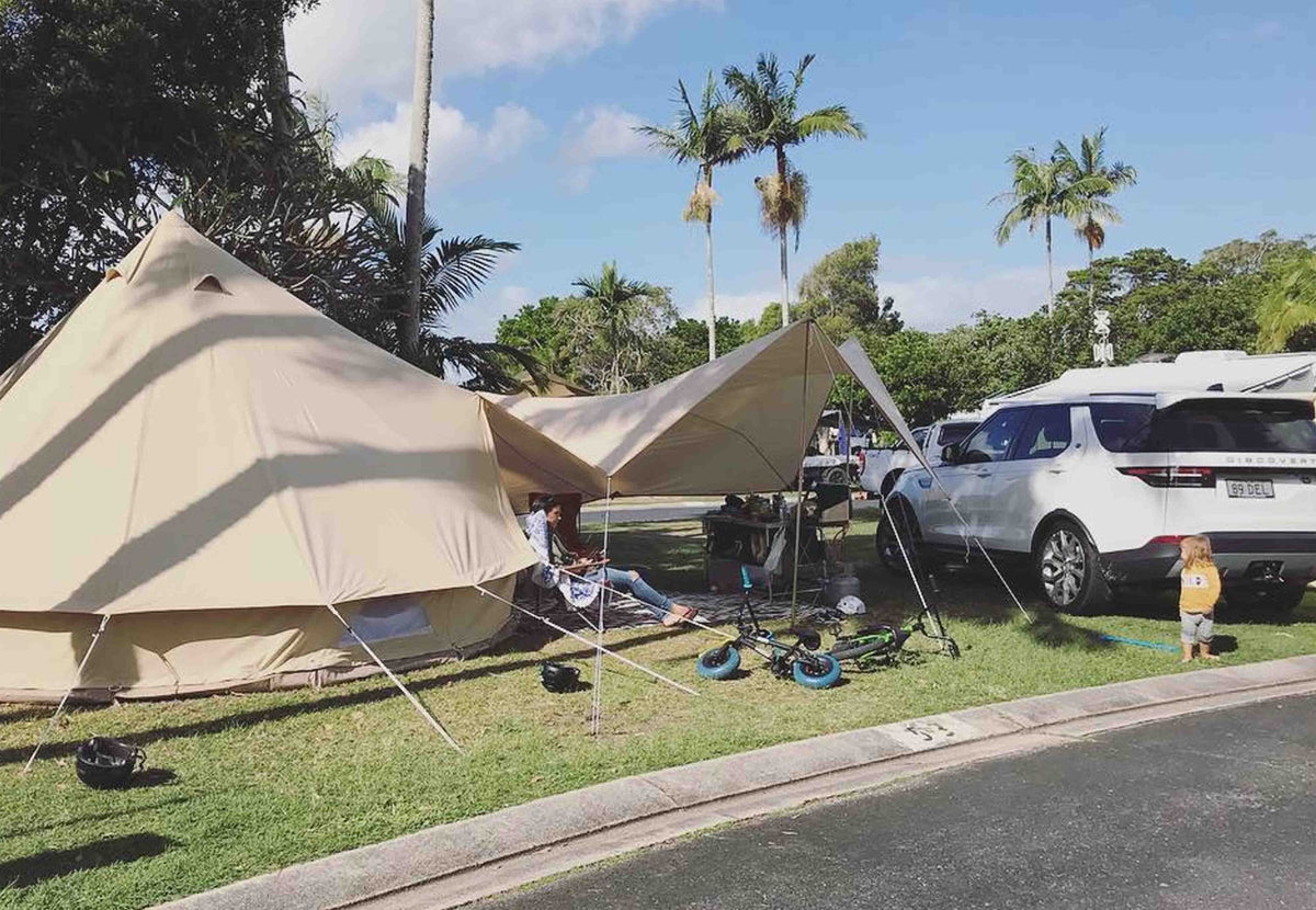 Auvent CanvasCamp Malu fixé à une tente cloche dans un camping avec des palmiers