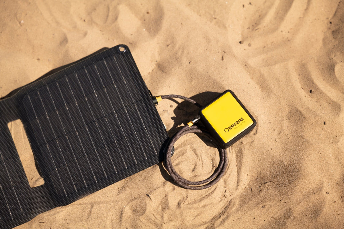 WakaWaka Power 10 dans le sable, relié à un panneau solaire pliable noir