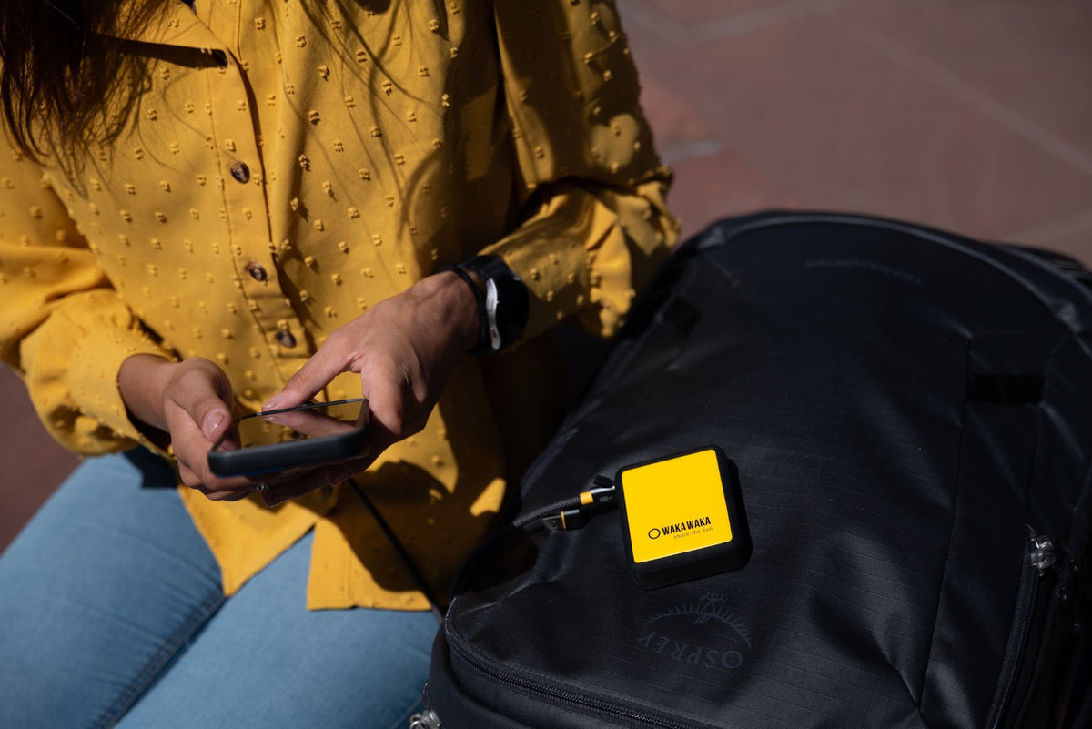 WakaWaka Power 20 sur un sac à dos noir, avec un câble relié au téléphone d'une femme