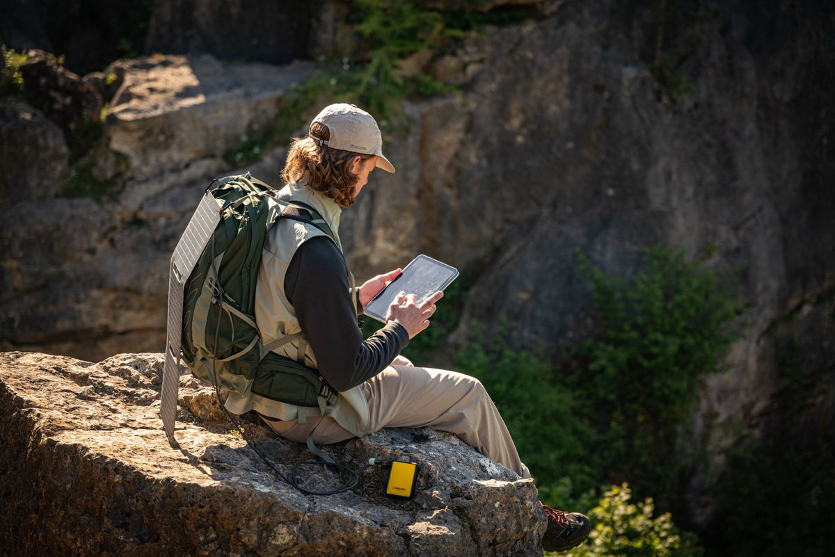 WakaWaka Power 20 sur un rocher à côté d'un randonneur avec sac à dos utilisant une tablette