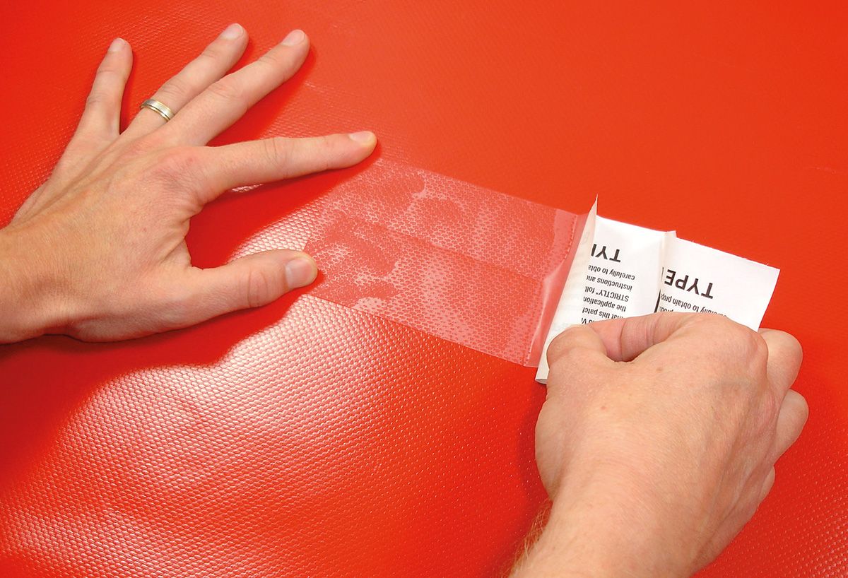 Patch Tear-Aid B appliqué à deux mains sur une toile PVC rouge