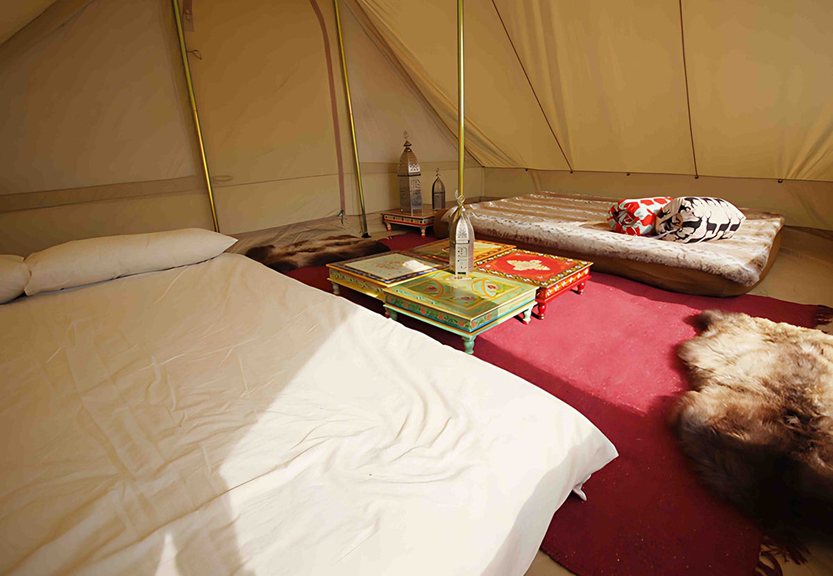 CanvasCamp Roman Traveller aménagée avec un lit, un tapis rouge et des tables basses colorées