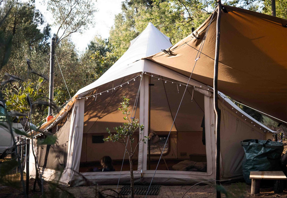 CanvasCamp Sibley Apex 520 Panorama avec façade ouverte, guirlande lumineuse et bâche entre les arbres