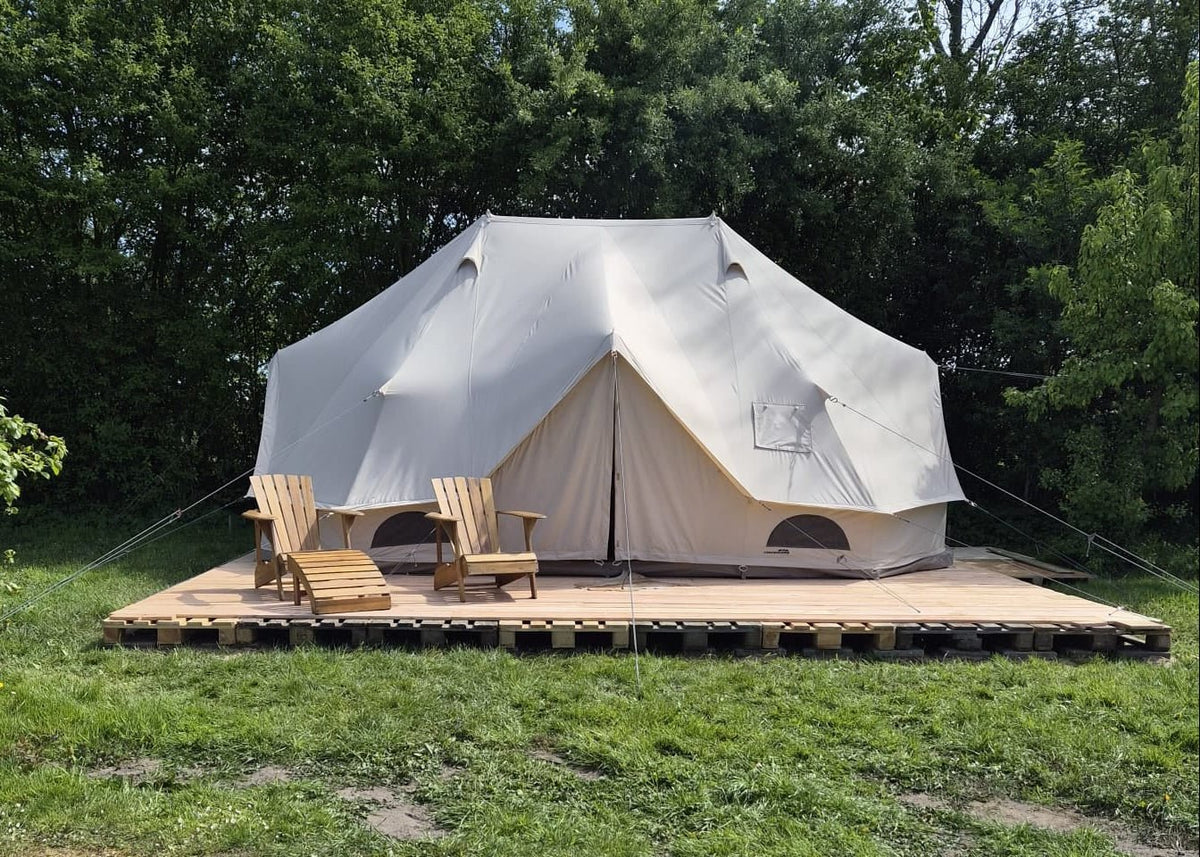CanvasCamp Sibley Apex 600 Twin sur une plateforme en bois dans l'herbe avec deux chaises de jardin en bois