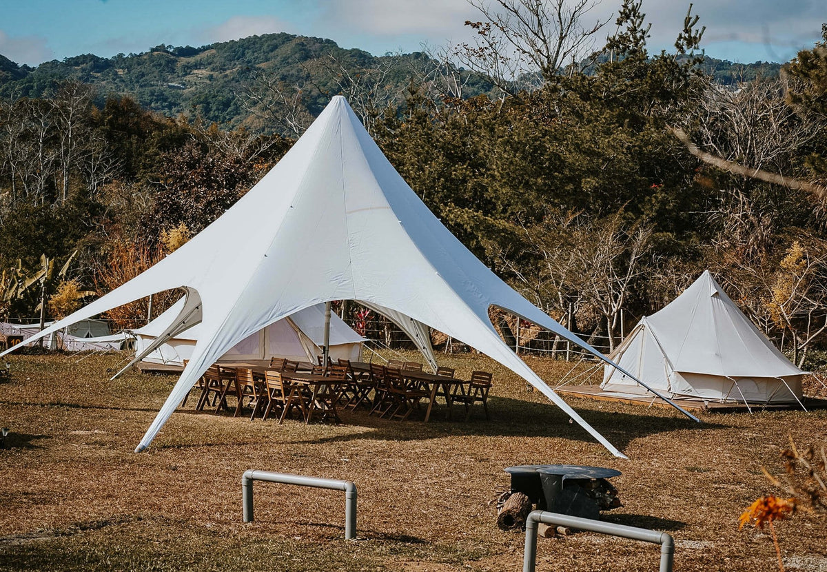 Tente événementielle CanvasCamp StarShade avec tables de pique-nique dessous, sur une pelouse près des collines