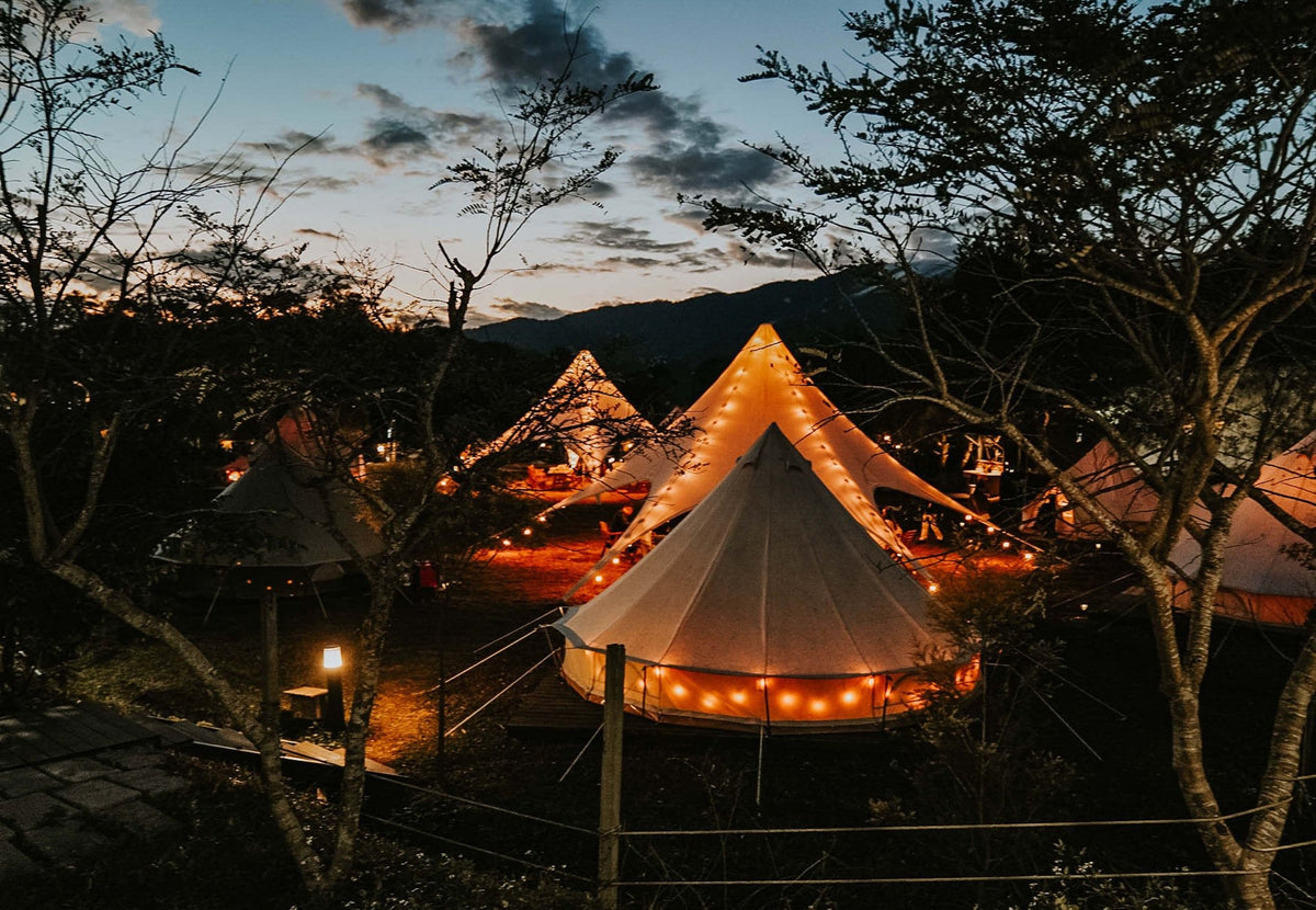 Tente événementielle CanvasCamp StarShade avec guirlandes lumineuses le soir, au-dessus d'une tente cloche éclairée