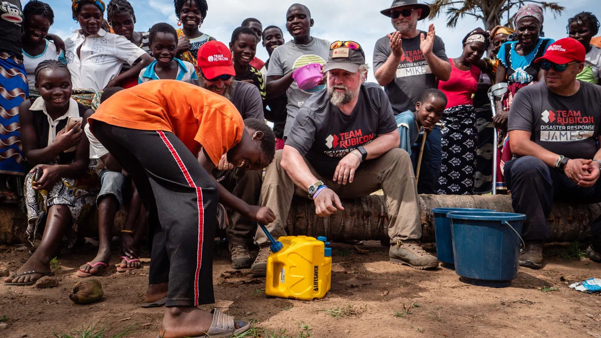 Water en filteren: een jongen bij een gele jerrycan en blauwe emmers, omringd door een groep toeschouwers