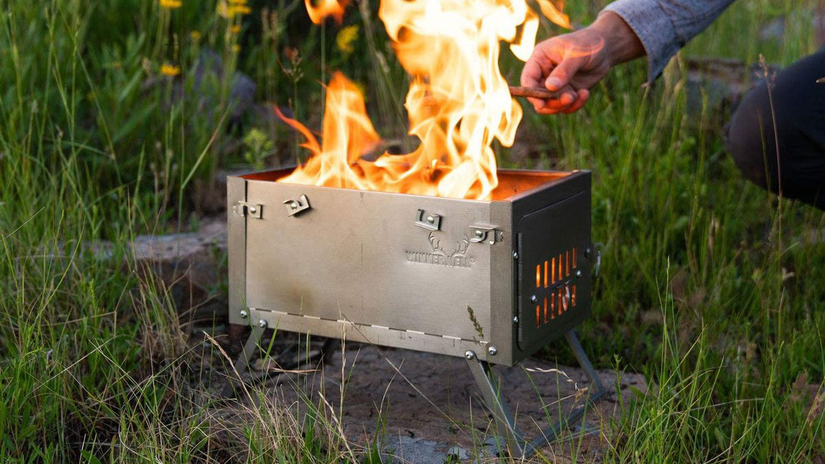 Buitenhaarden, stalen vuurkorf op pootjes met brandend hout in het gras