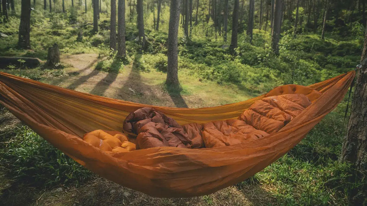 Kampeerartikelen, oranje hangmat met een slaapzak erin tussen de bomen in een bos