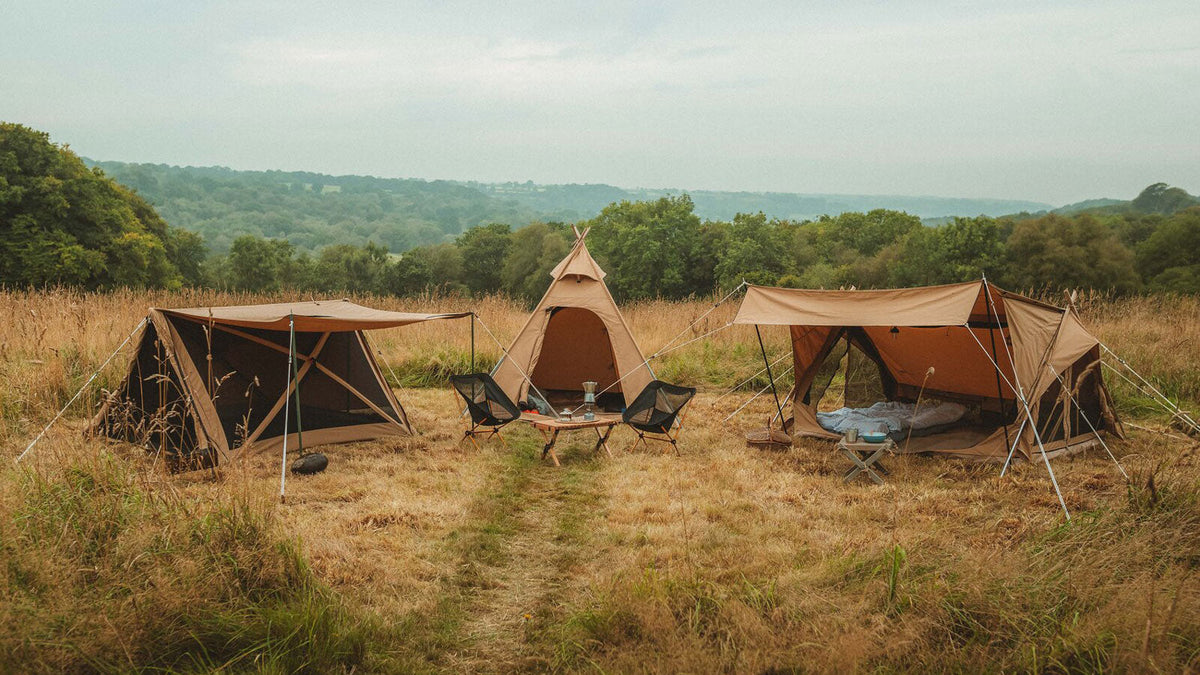 Compacte tenten, drie bruine tenten met luifels en stoelen op een grasveld in de heuvels