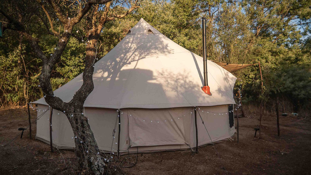 Apex tenten, grote beige canvas tent met schoorsteenpijp tussen de bomen