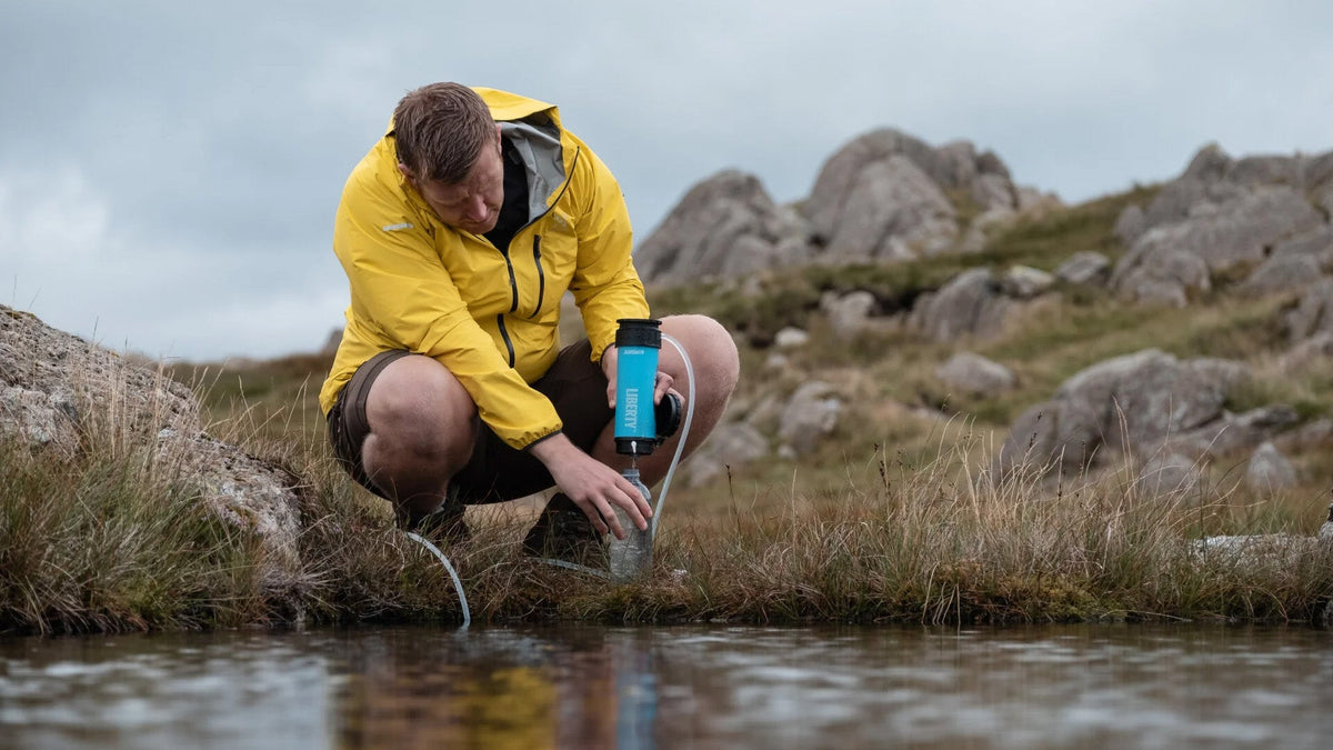 Draagbare waterfilters en zuiveringstoestellen, wandelaar filtert beekwater in een blauwe fles