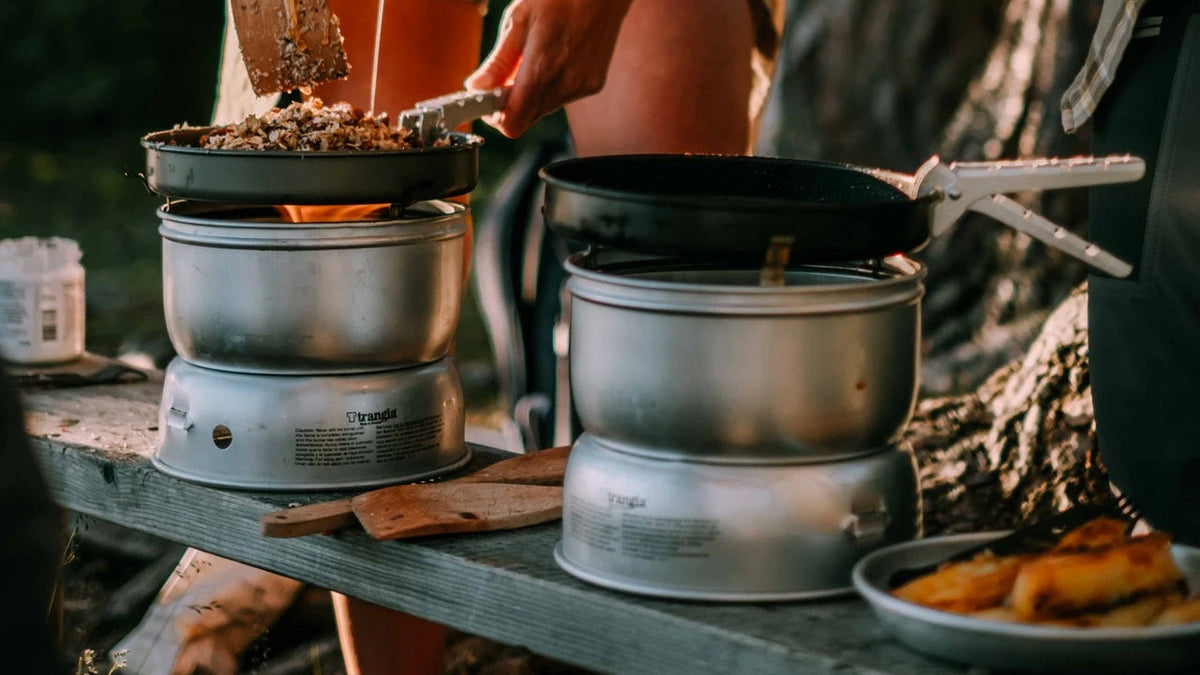 Koken en pannensets, twee kampeerbranders met pannen en koekenpannen op een houten bank