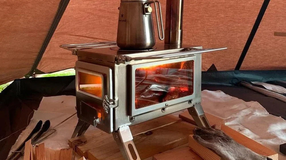 Nomad tentkachel met glazen deur en zijruit, brandend vuur en een waterketel in een tent