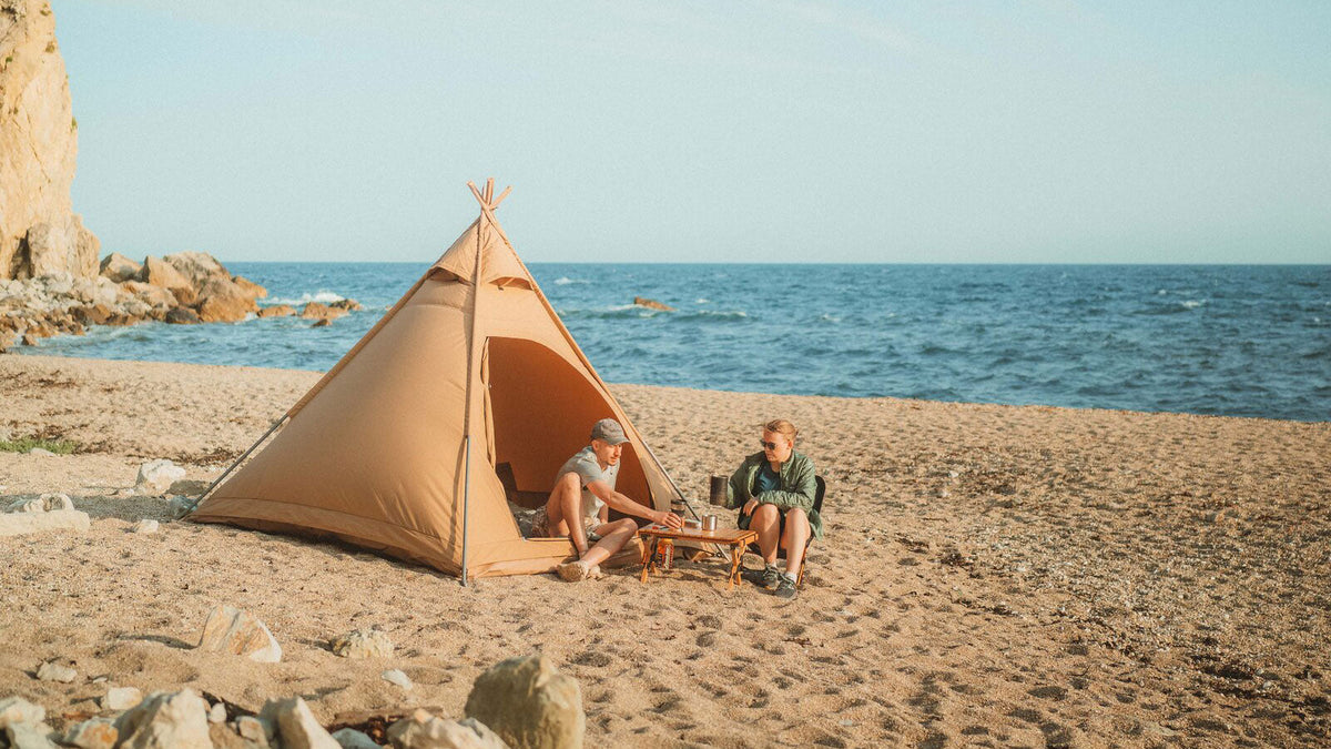 Piramidetenten, beige piramidetent op het strand met twee mensen aan een tafeltje bij zee