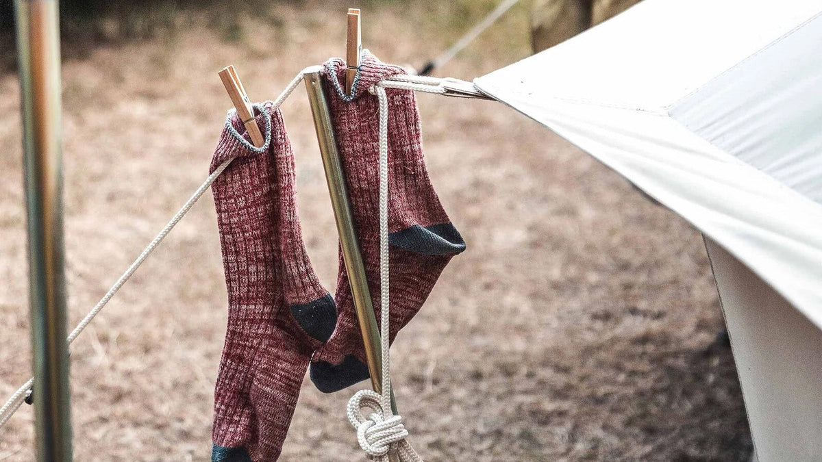 Tentstokken, rode wollen sokken met knijpers aan een lijn bij een houten tentstok en tarp