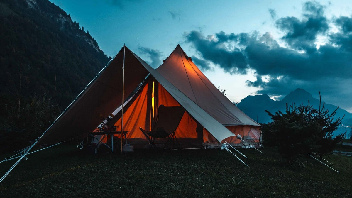 Luifels, twee verlichte bell tents met een luifel ertussen in de bergen bij schemering