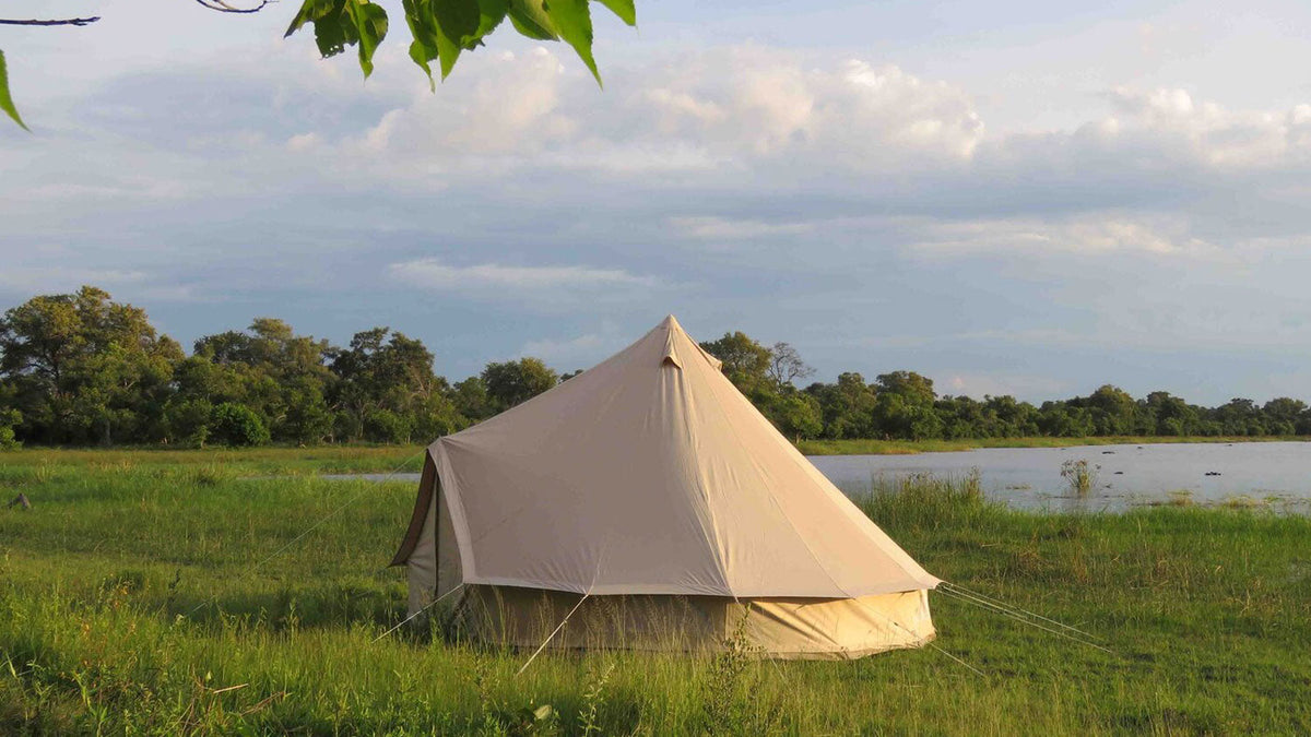 CanvasCamp Traveller, beige bell tent op een grasveld aan een meer met bomen