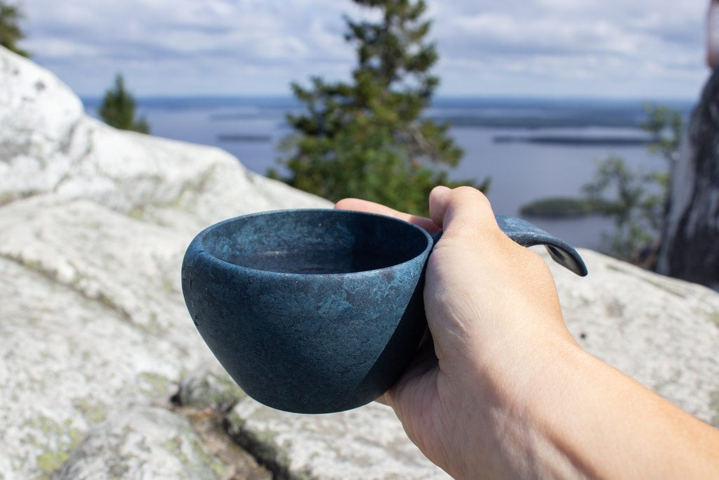 Kupilka 21 Classic Cup bleue tenue en main sur un rocher avec vue sur un lac