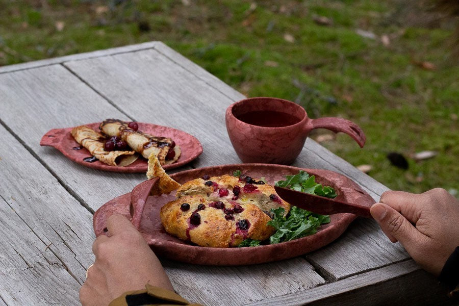 Kupilka 44 assiette rouge avec feuilleté salé et salade sur une table en bois dehors, près d'une tasse rouge