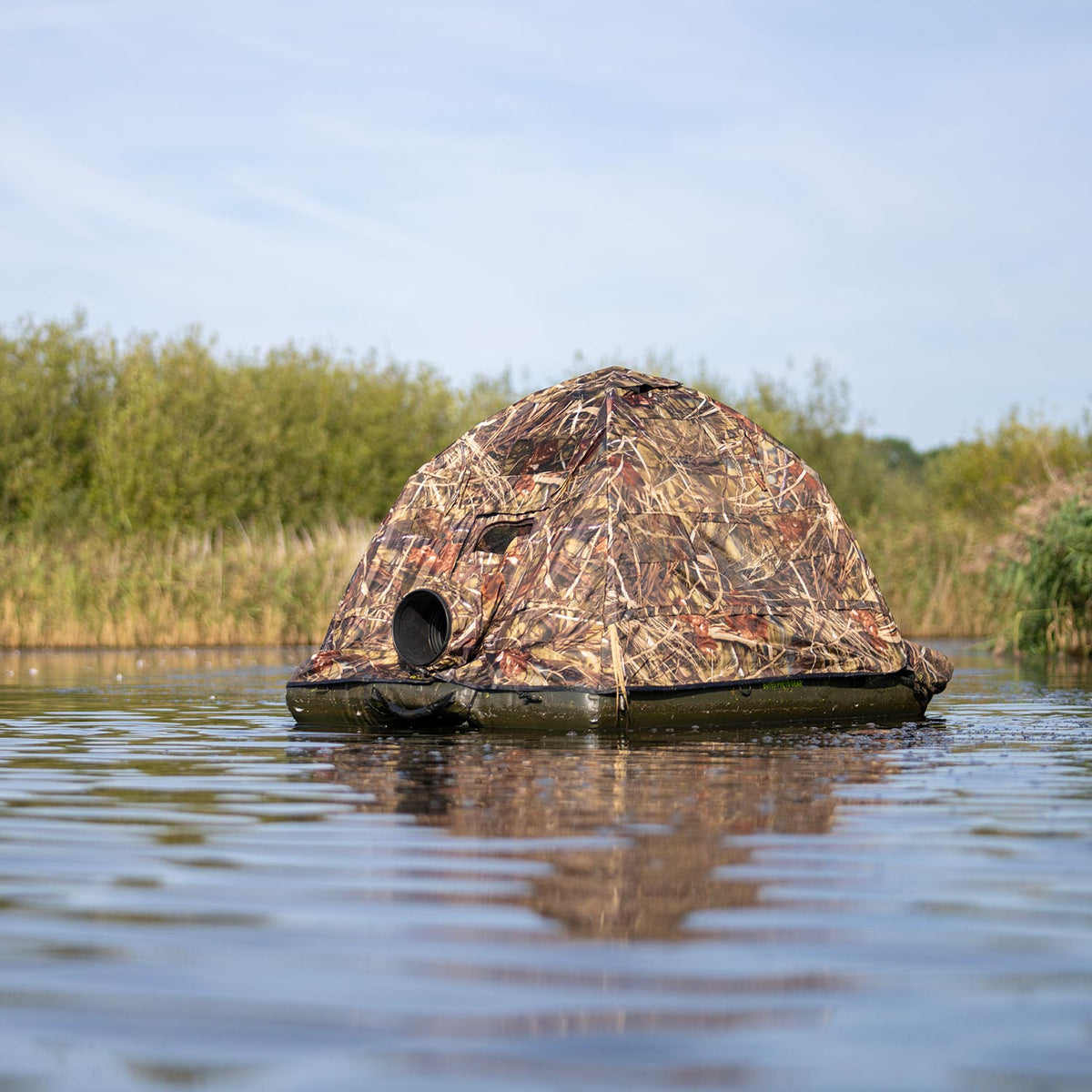Affût flottant Buteo Grebe de face sur l'eau, ouverture ronde pour objectif et roseaux en arrière-plan