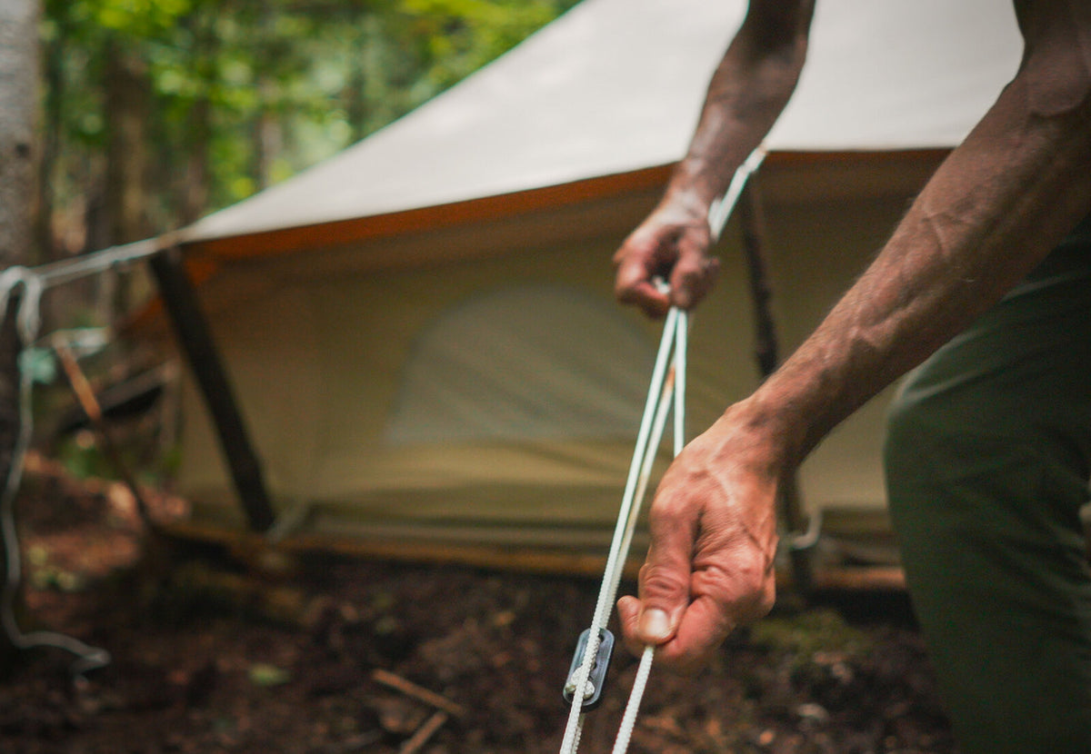 Haubans CanvasCamp en cours de tension sur une tente en toile dans la forêt