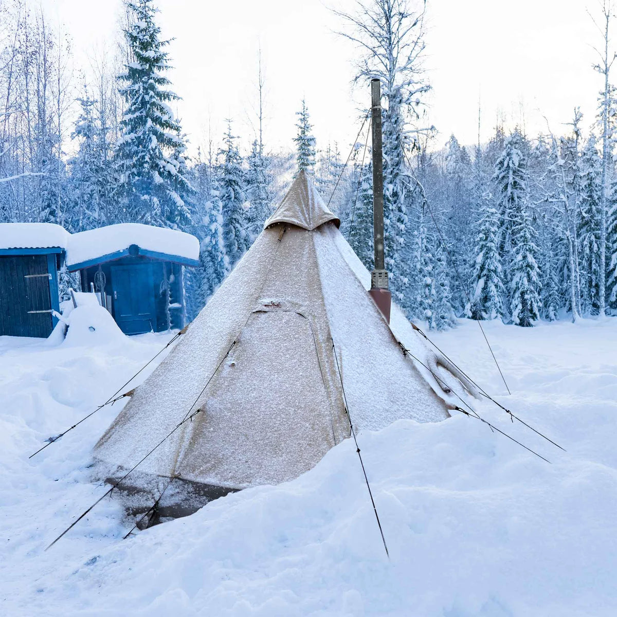 Tente tipi Winnerwell Arctic avec tuyau de poêle dans la neige entre des pins enneigés