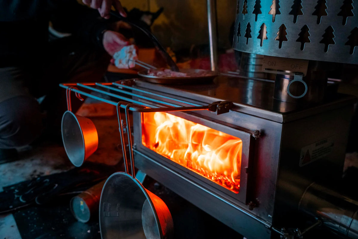 Winnerwell Nomad Plus Double View en service avec le feu derrière la vitre latérale et des casseroles sur l'étagère
