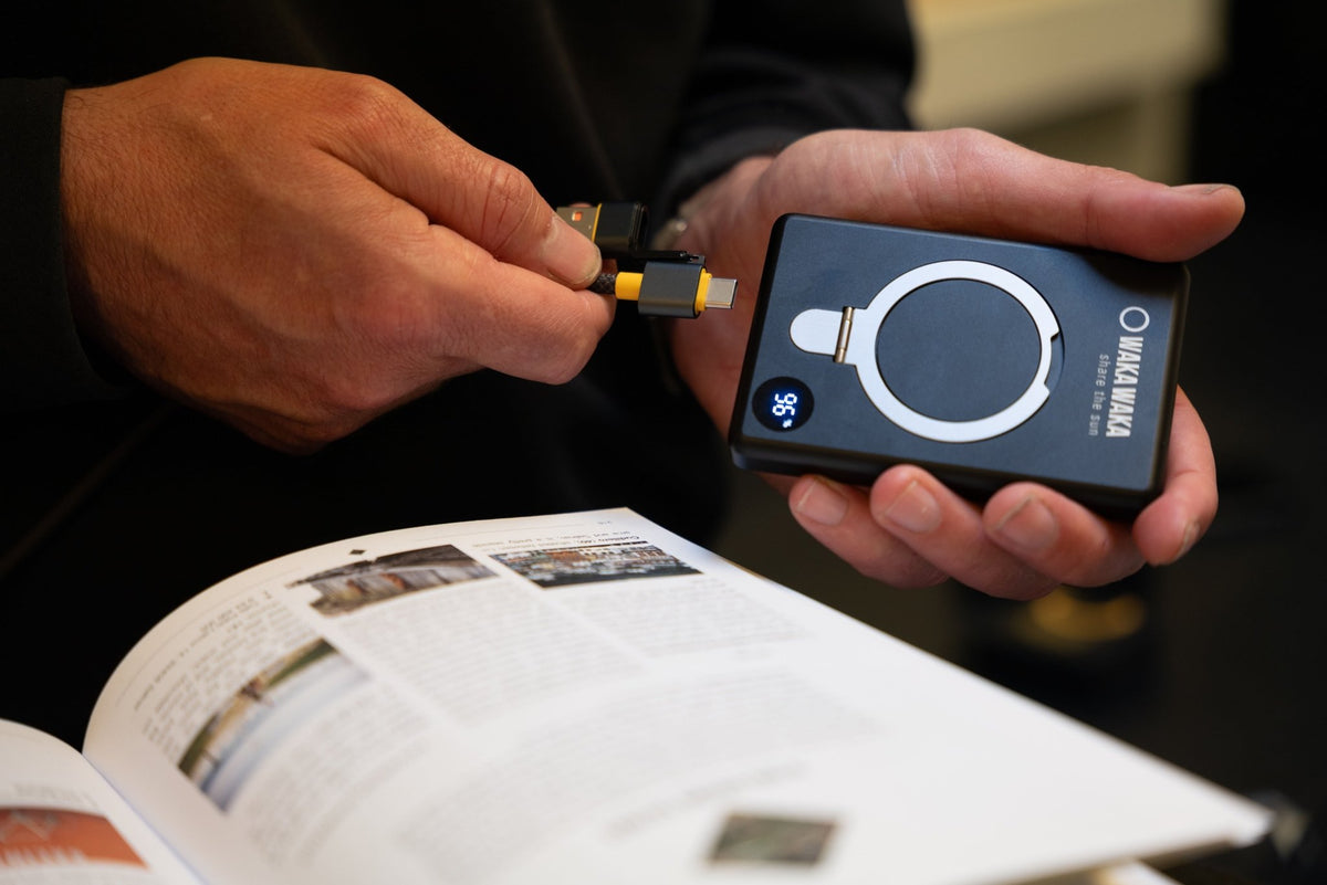 WakaWaka Power Pro noir tenu en main pendant qu'on branche un câble, au-dessus d'un livre