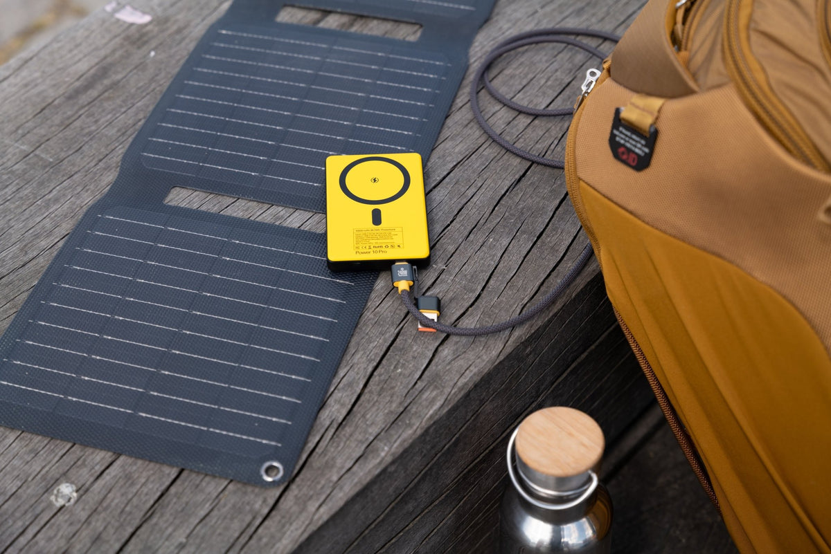 WakaWaka Power Pro jaune sur un panneau solaire pliable posé sur un banc en bois à côté d'un sac
