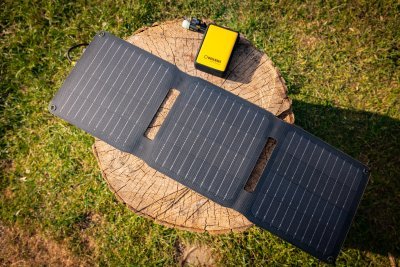WakaWaka Solar 20 vu de dessus sur une souche d'arbre dans l'herbe, avec une batterie externe jaune