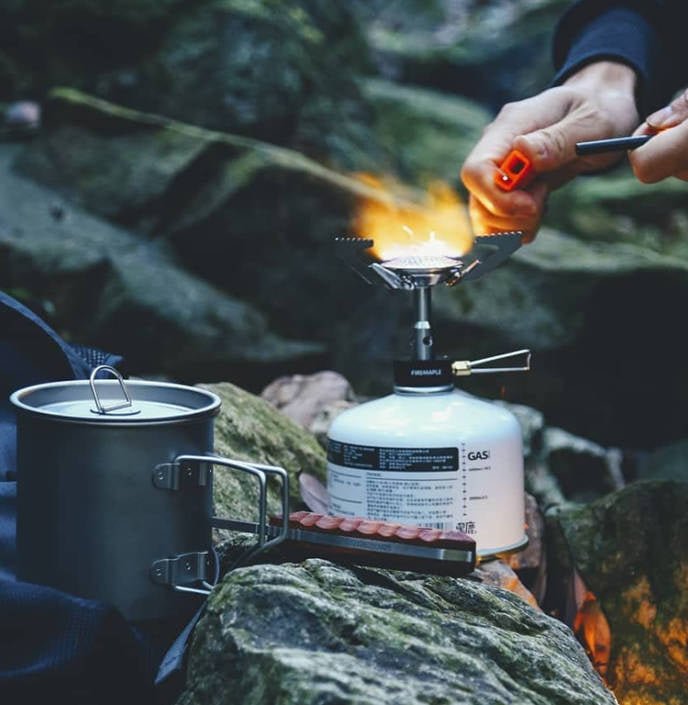 Fire Maple BUZZ sur une cartouche entre les rochers, allumé avec un briquet, casserole à côté