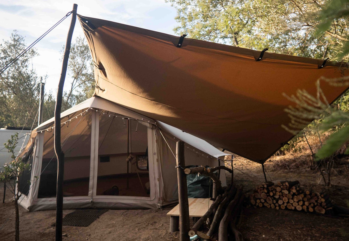 CanvasCamp Heavy Duty Shelter marron tendu au-dessus d'une tente avec un tas de bois à côté